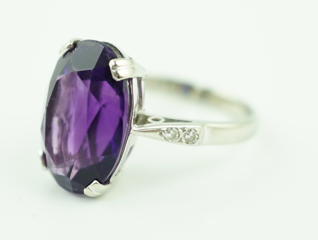 An 18ct white gold and oval cut amethyst set ring, with two stone diamond chip set shoulders